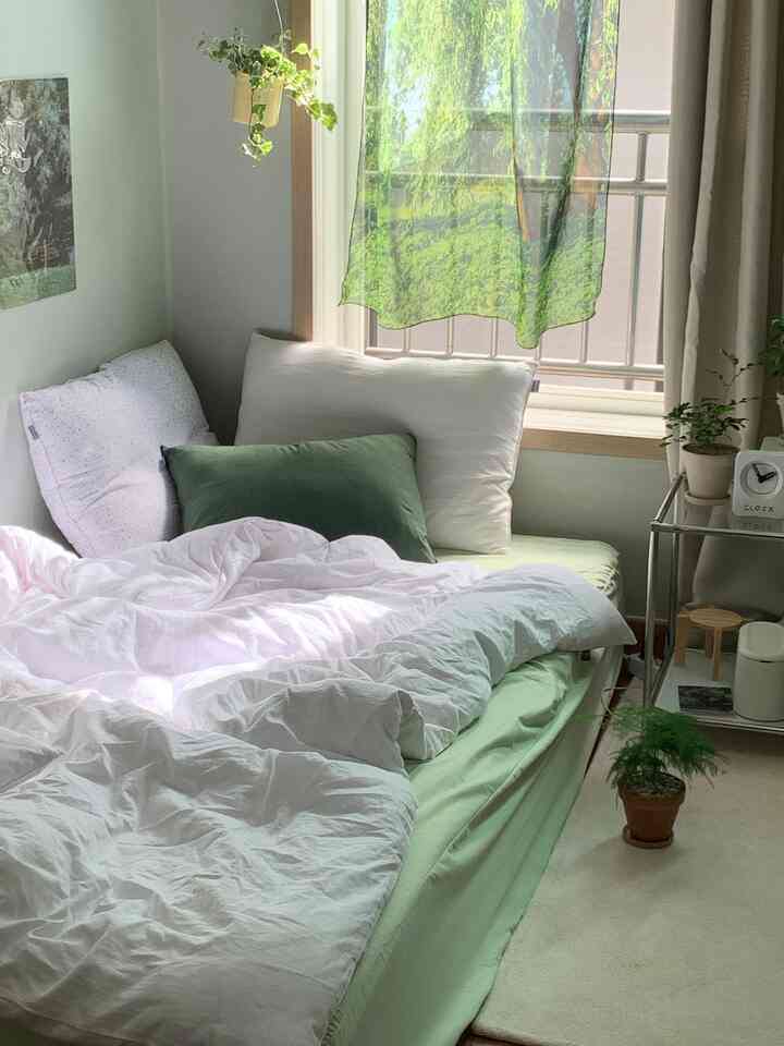 白と緑のトーンの寝室、窓辺にカーテンと植物が配置されて落ち着いた雰囲気のあるインテリア