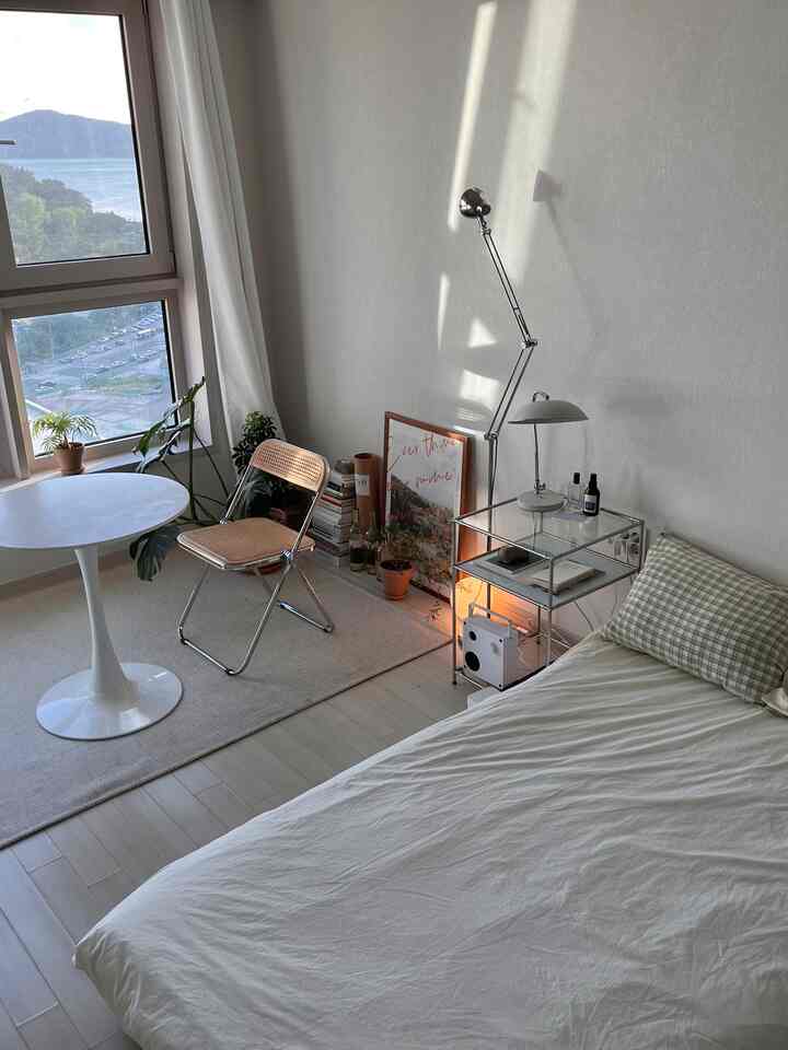 ホワイトとナチュラルカラーの寝室、ラタンチェアとナイトテーブル、植物が配置された落ち着いた雰囲気のインテリア