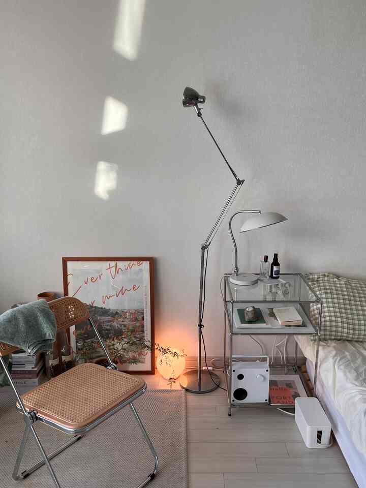 シンプルでナチュラルな雰囲気の寝室、シルバーのフロアランプとラタン折りたたみ椅子が配置された印象的な空間