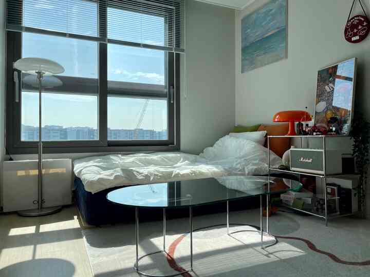 明るいホワイトトーンの壁とベッド、黒いガラスのコーヒーテーブルとフロアランプが配置された落ち着いた寝室のインテリア