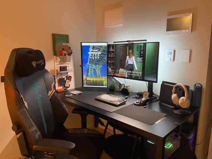 ブラックとネイビートーンのホームオフィス兼ゲームルーム、デュアルモニターとゲーミングチェアが配置された整然とした作業空間