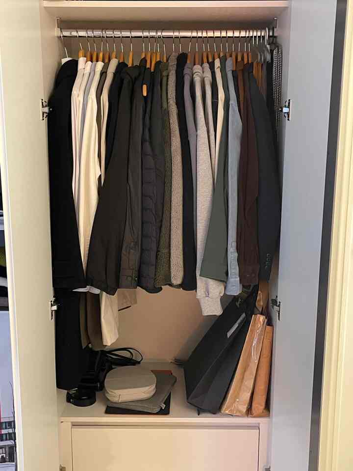 白を基調としたコンパクトなクローゼットに、木製ハンガーで整然と掛けられた服がある実用的な収納スペース