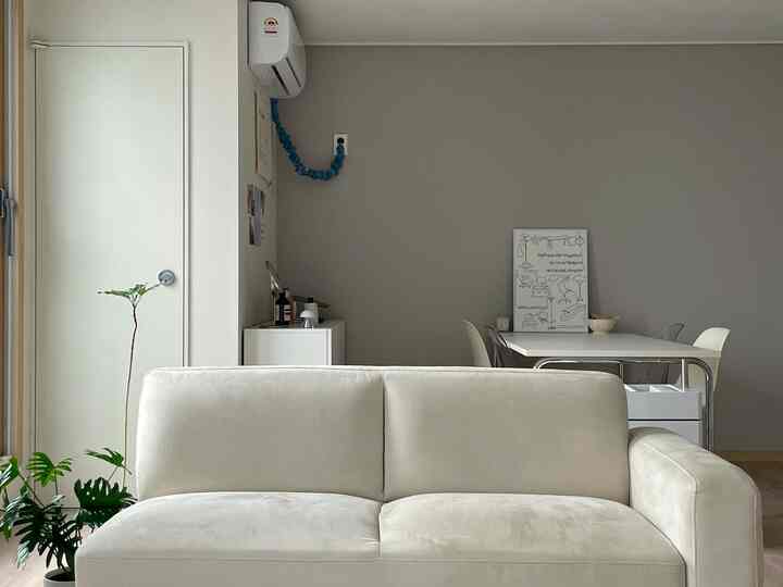 ナチュラルなベージュと白の色調のリビング、中央に3人掛けソファと透明な椅子が配置されたすっきりとした空間