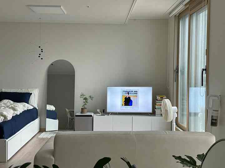 ホワイトとネイビートーンのリビング、シングルソファとベッド、テレビ収納が配置されたシンプルモダンな印象的な空間