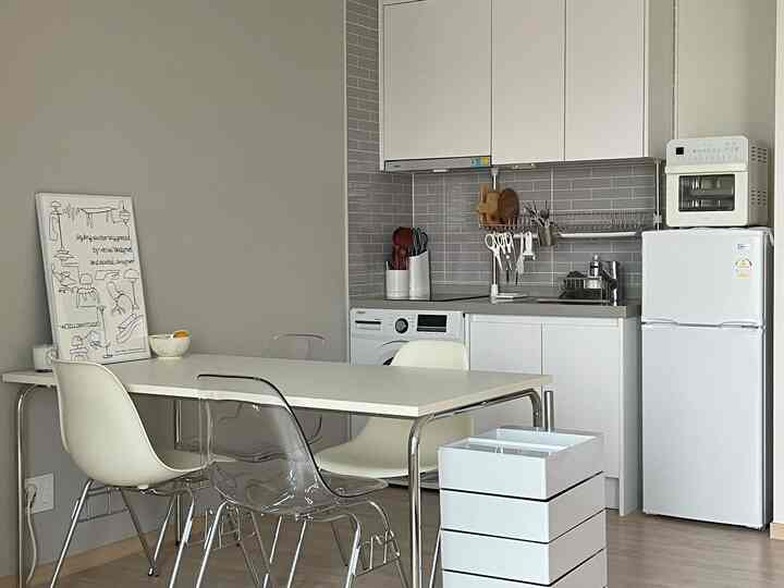 白を基調としたキッチンスペース、透明な椅子とダイニングテーブルが配置された清潔でコンパクトなインテリア