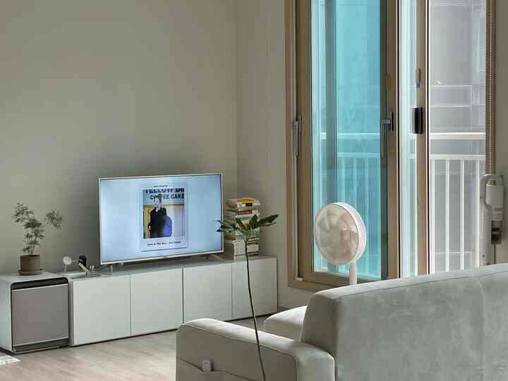 ホワイトとナチュラルカラーのワンルームリビング、ソファとテレビ台、扇風機が配置されたシンプルでモダンな空間