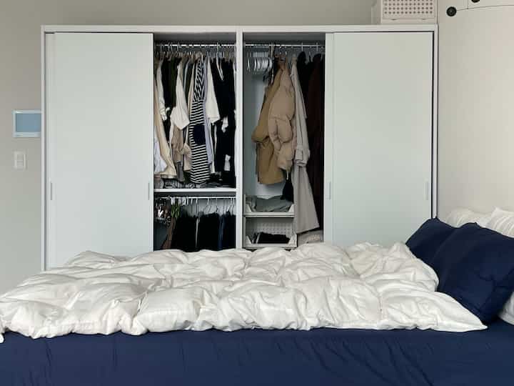 白とネイビーの色調の寝室、白いスライディングドアのクローゼットと整頓されたベッドが配置された落ち着いた空間