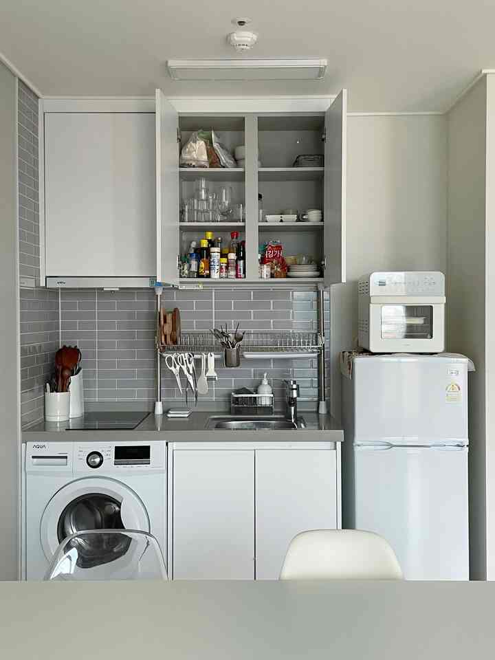 白とグレーのトーンでまとめられたコンパクトなキッチン、収納棚が開き多様なキッチン用品が整頓されたモダンなインテリア