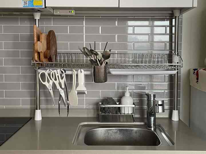 グレーのタイル壁とステンレス製の柱式食器乾燥ラックが設置されたキッチンのシンクスペース。