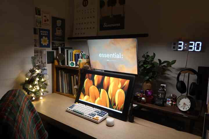 ナチュラルな色調のホームオフィスのワークスペース、クリスマスのミニツリー、モニター、液晶タブレットが配置された居心地の良い空間