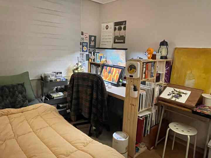 黄色の布団がある寝室と壁にポスターが配置されたホームオフィスが一体となった雰囲気のある部屋