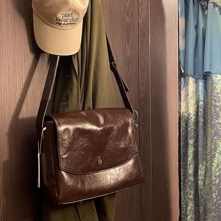 ブラウンのレザー製バッグとオリーブ色の衣服が掛けられた玄関、自然の風景柄のカーテンが配置された雰囲気のあるインテリア