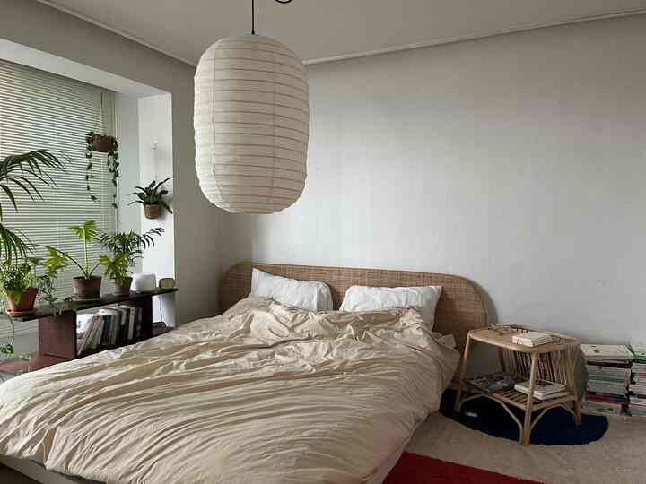 ベージュとホワイトの色調の寝室、自然素材のベッドとサイドテーブル、窓際に植物が配置された雰囲気のあるインテリア