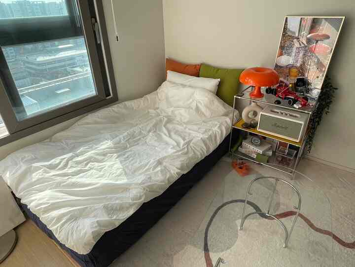 ホワイトとナチュラルトーンの寝室、白い寝具とモジュール式ナイトテーブル、オレンジとグリーンのクッションがアクセントの清潔感あるインテリア