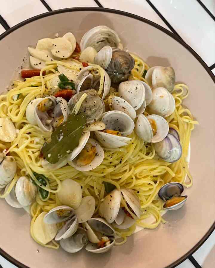 ベージュ色の皿に盛られた貝とパスタの料理、シンプルなホームクックの食卓風景