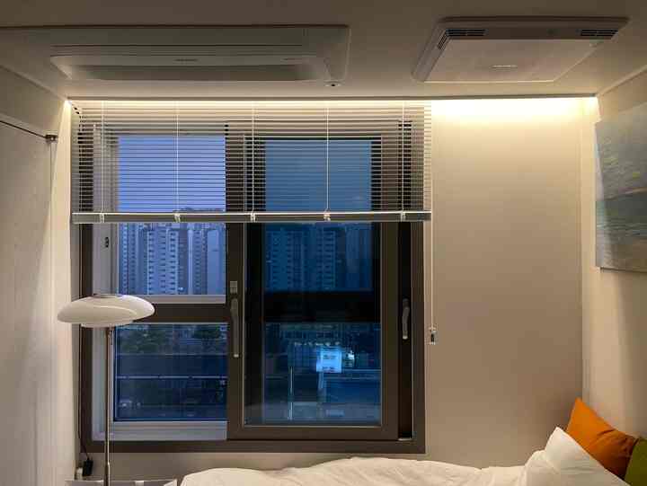 白とベージュの色調の寝室、窓に白いブラインドとフロアランプが配置された落ち着いた雰囲気のインテリア