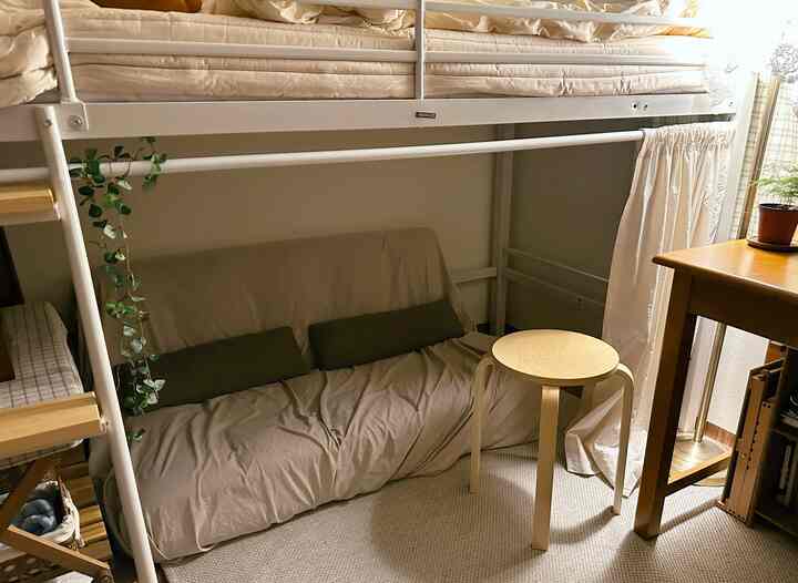 ベージュとナチュラルウッド調のロフトベッド下スペース、ソファと木製サイドテーブルが配置された雰囲気のあるインテリア