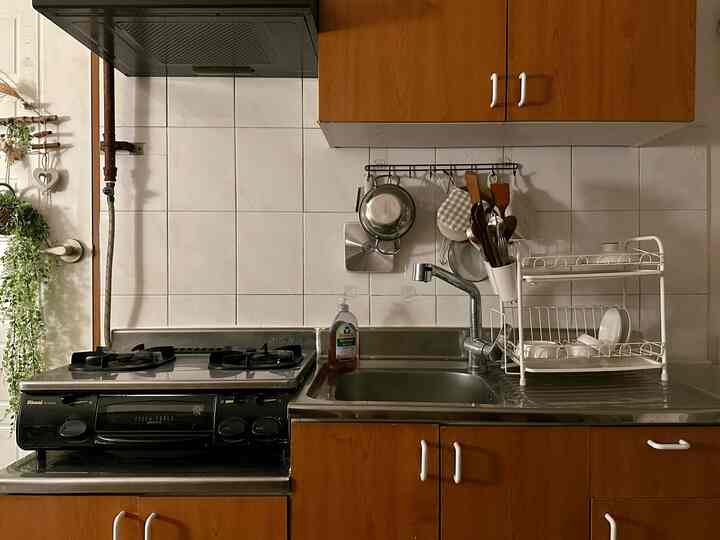 白いタイルと茶色の木製収納がある狭くて整頓されたキッチン、シンクと食器乾燥ラックが配置された空間