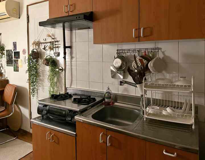 白いタイル壁と木目調のキッチン家具が調和したシンプルなキッチン、ガスコンロとシンクが見える