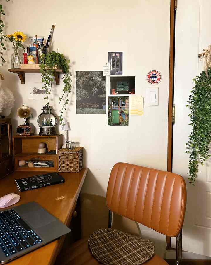 ブラウンレザーの椅子と木製デスクが配置されたナチュラルカラーのホームオフィス、壁には植物とポスターが飾られた雰囲気のあるインテリア