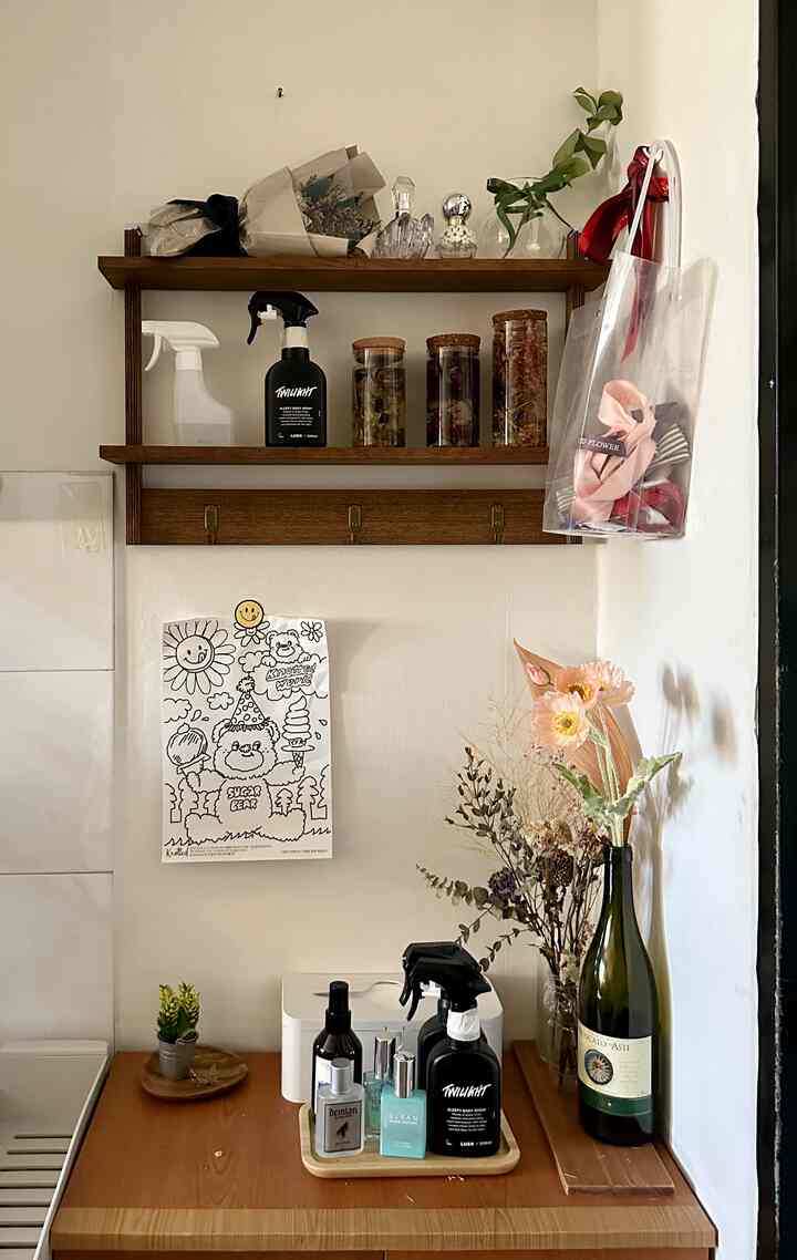 ナチュラルな色調の玄関、木製のシューズラックと壁棚に整頓された香水と花が配置された雰囲気のあるインテリア