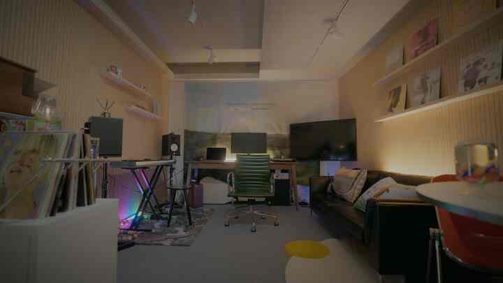 ナチュラルトーンのワークスペース、デスクとグリーンのオフィスチェア、黒のレザーソファ、電子キーボードが配置された機能的な空間