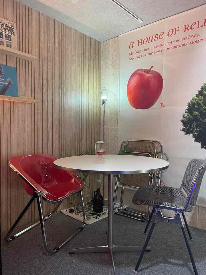 赤と白のトーンでまとめられたカフェ風ホームオフィス、丸テーブルと異なるデザインの椅子が配置され、ファブリックポスターとフロアランプが雰囲気を演出している