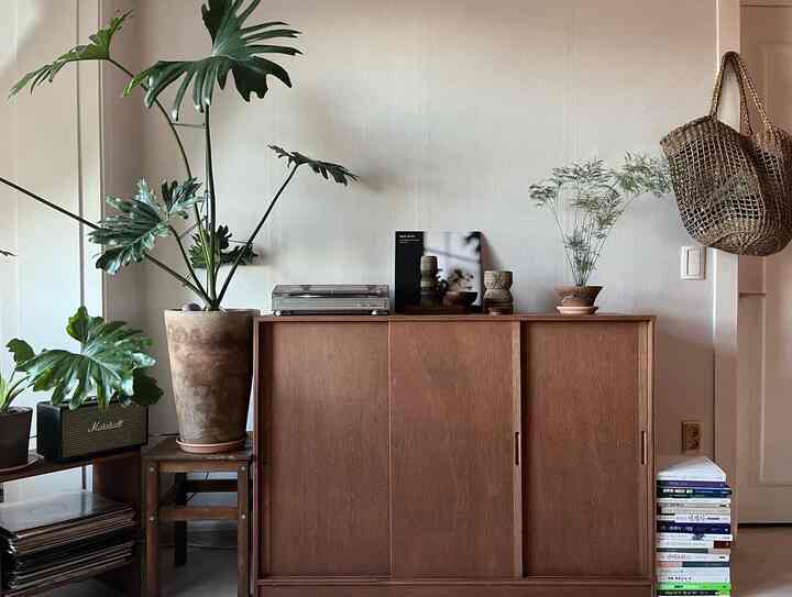 ナチュラルな色調のリビング、ラワン合板の収納キャビネットとイケアのスツール、大きな植物が配置された温かみのあるヴィンテージな雰囲気のインテリア