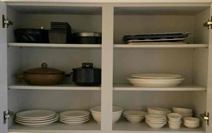 白と茶色のトーンのキッチンキャビネット内、さまざまなサイズのボウルや鍋が整然と並べられた印象的な空間