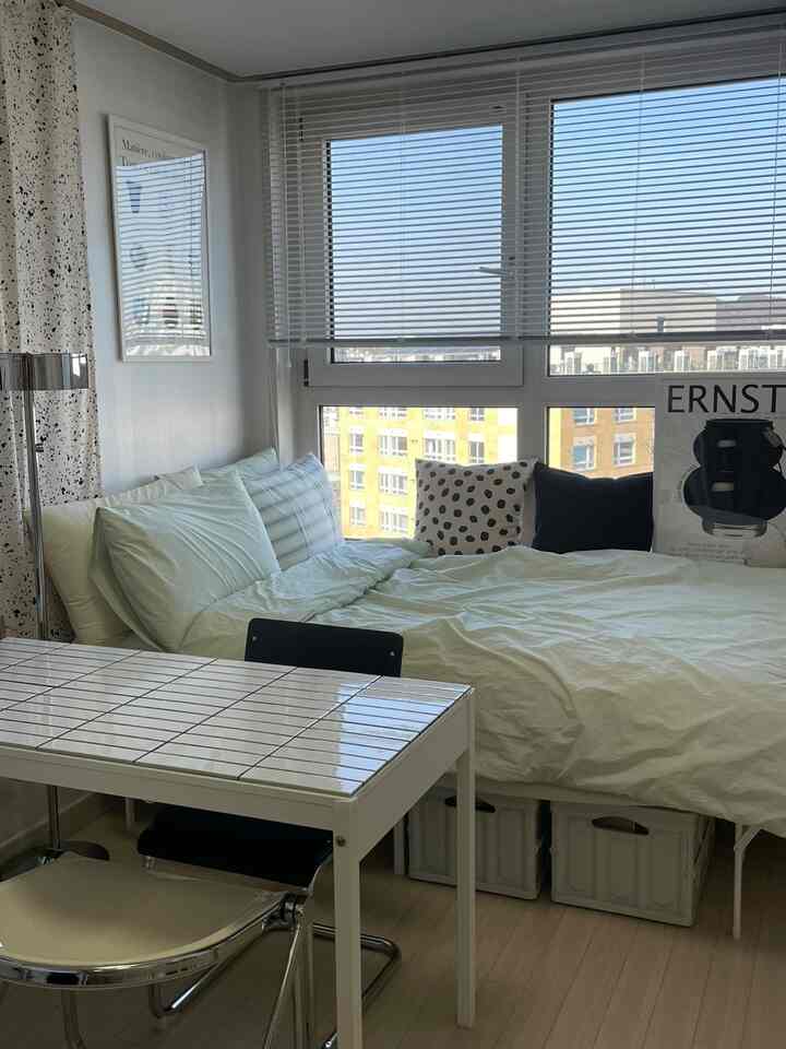 白とグレーのトーンの寝室、窓のブラインドと寝具が配置された一人暮らし向けの空間