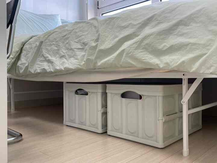 明るい木目調の床と白いベッドフレームの下に折りたたみ収納ボックスが配置された落ち着いた寝室空間