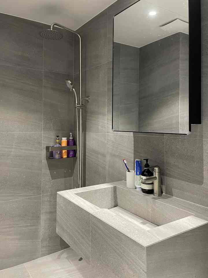 チャコールトーンのタイルで仕上げられた洗練されたホテルライクなバスルーム、大型の洗面台とレインシャワー水栓が配置された空間