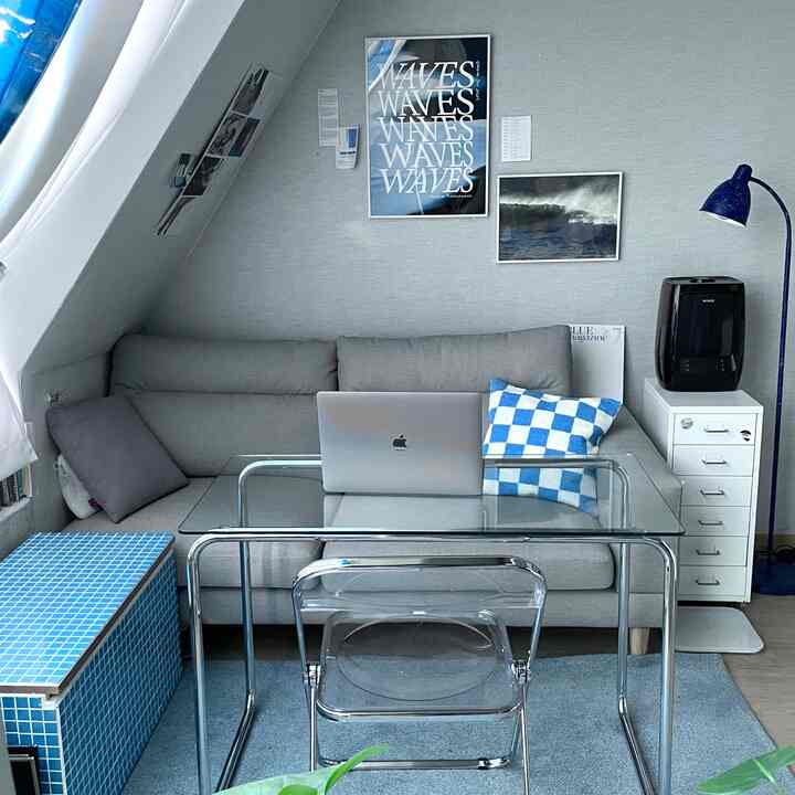 グレーとブルーのトーンのリビングルーム、ソファとクッション、透明なガラステーブル、青いタイルベンチが配置されたモダンな雰囲気の空間