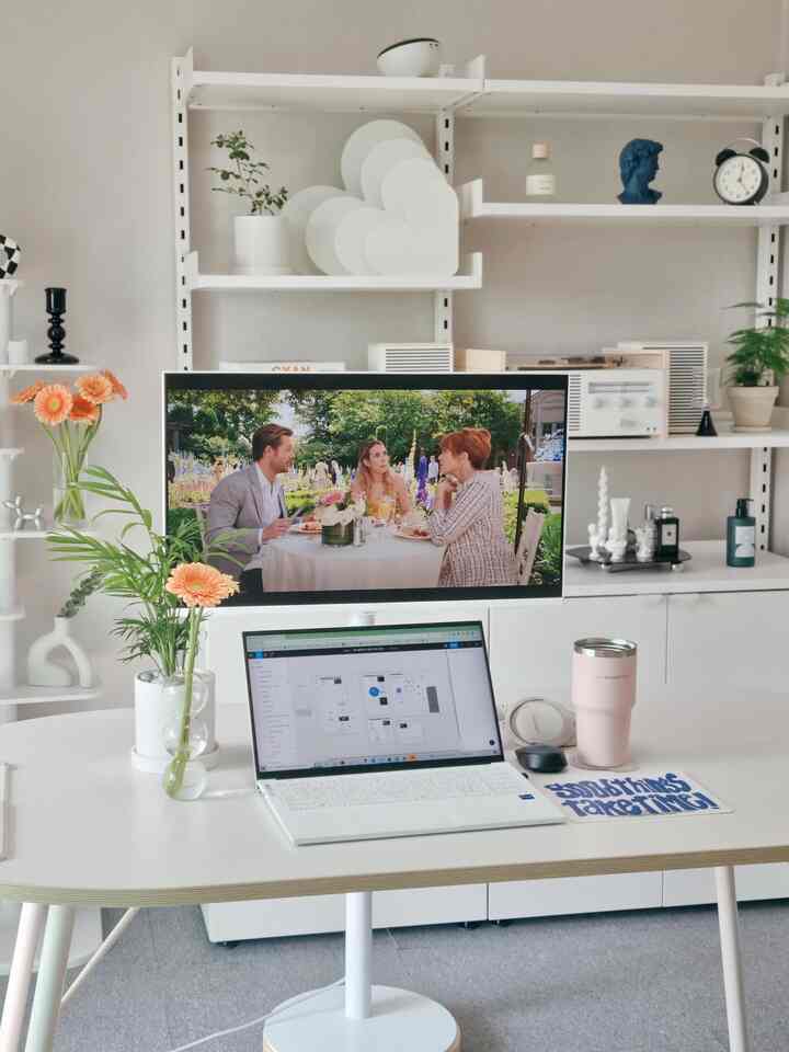 明るいホワイトトーンのリビングルーム、中央にノートパソコンとモニターがある白いデスクと多様な植物が配置された清潔感のあるホームオフィス