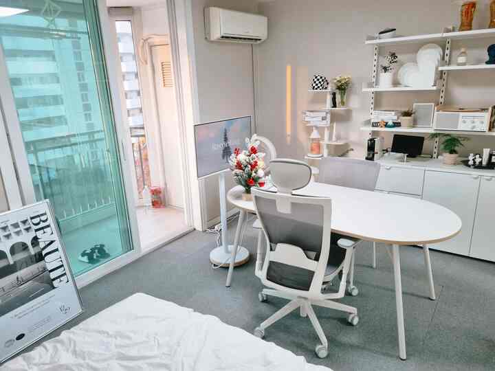 白を基調としたリビングスペース、中央に白い楕円形のデスクとメッシュのオフィスチェアが配置された清潔感のあるモダンなホームオフィスの雰囲気