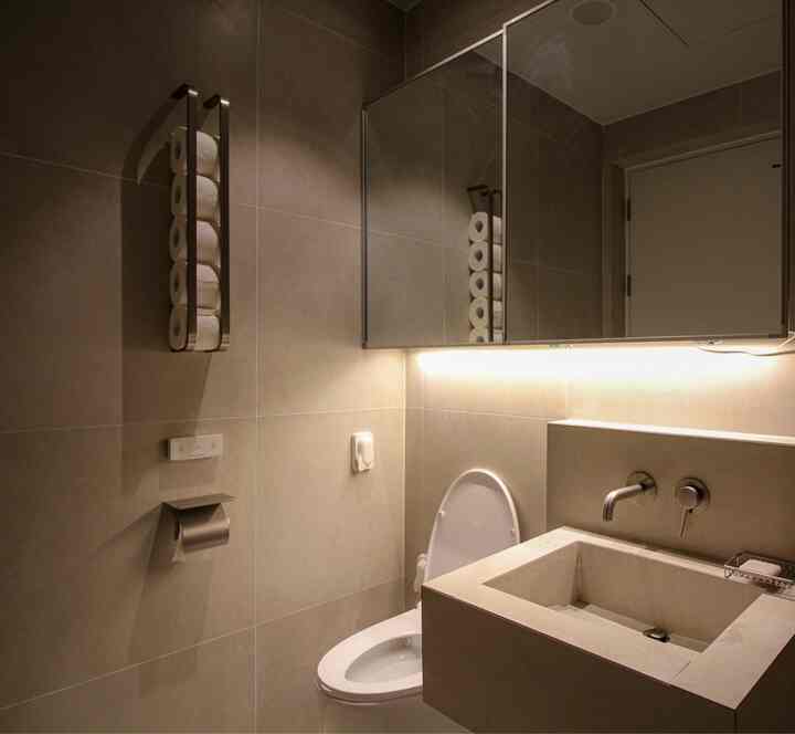 ベージュ色調のモダンなバスルーム、ステンレス製タオル掛けと間接照明が配置された清潔な空間