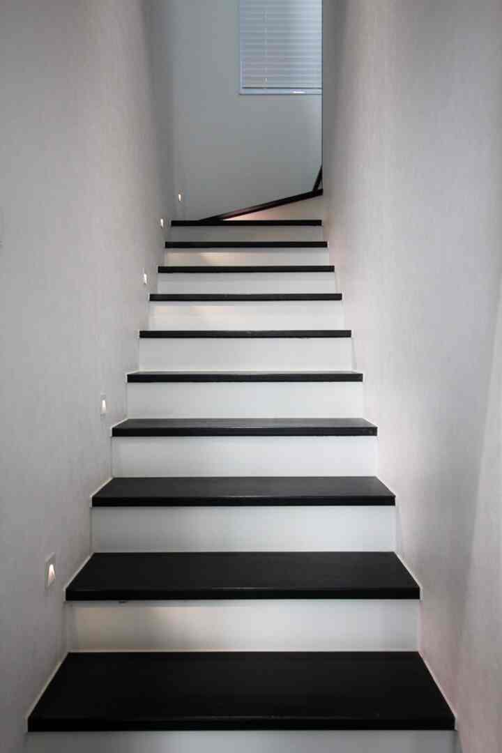 白い壁と黒の階段踏み板が調和したモダンな階段室、壁のストリングライトがアクセントとなっている空間