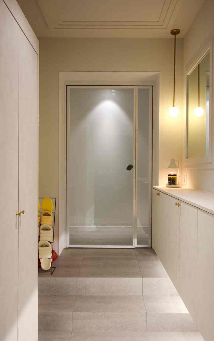 暖かいホワイトとウッドトーンの段差のあるモダンな玄関、整頓された靴収納とキャビネット、キャンドル照明が配置された落ち着いた空間