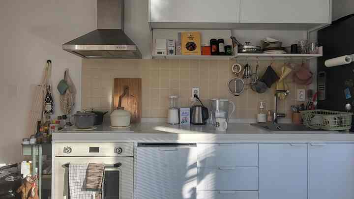 ベージュのタイル壁とホワイトの下部・上部キャビネット、オープンシェルフが配置されたコンパクトで清潔感のあるキッチン