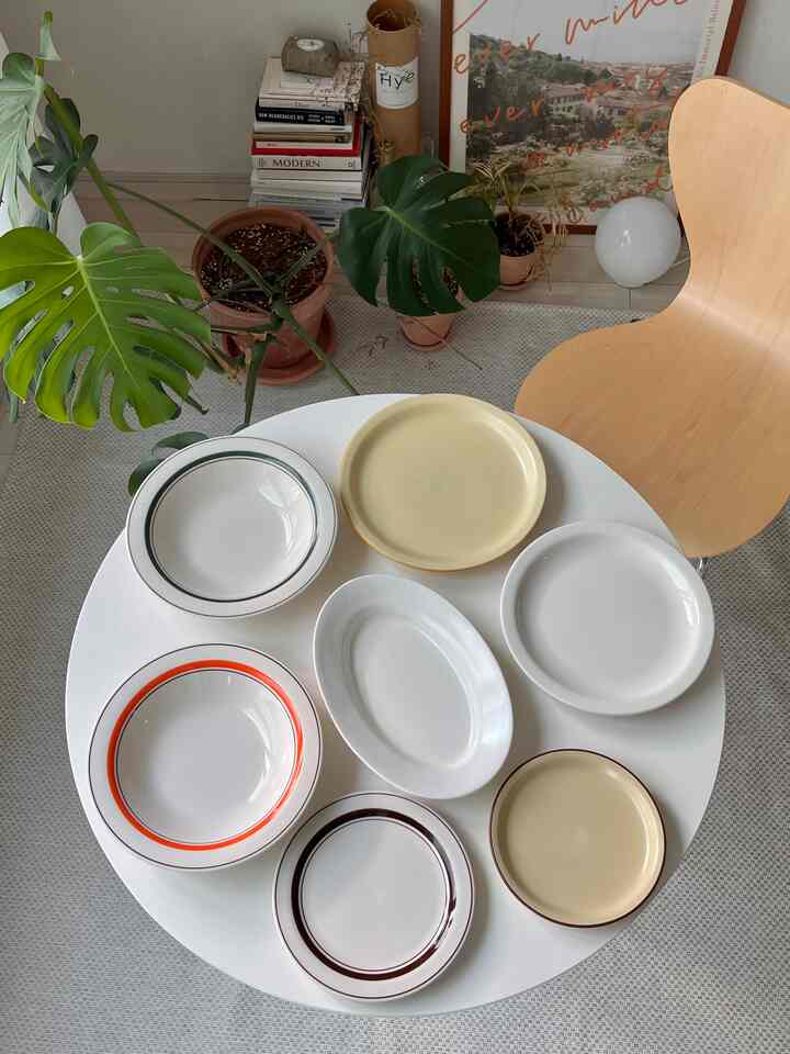 白とベージュのトーンが特徴の丸いテーブルに様々な皿が並び、緑の植物が配置された雰囲気のあるインテリア