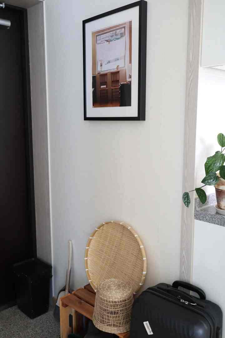 明るい白色の壁にイケアの額縁が掛けられ、木製の箱と竹ざる、ラタン鉢カバーが置かれた玄関の自然な収納空間