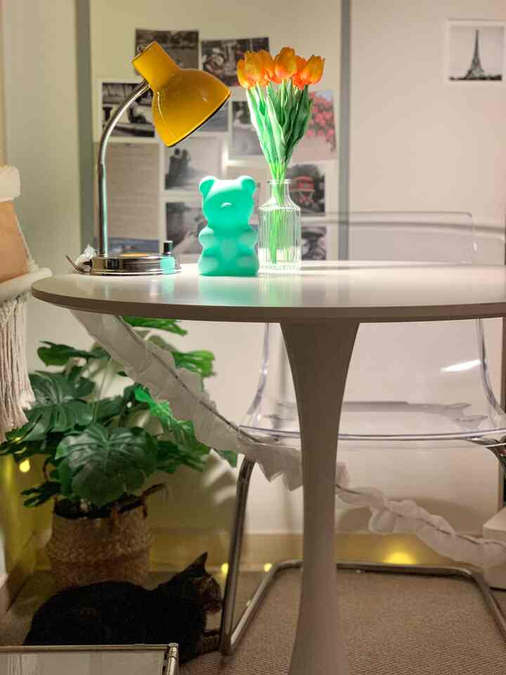 白を基調とした居心地の良いリビング空間、黄色の作業用ランプとムードライト、テーブルのチューリップ花瓶が温かみを演出する