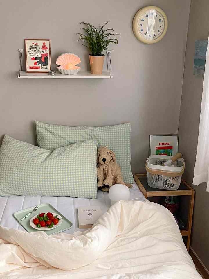 ベージュ色の壁と居心地の良い寝室、チェック柄の枕と装飾が置かれたナイトテーブルが調和する空間