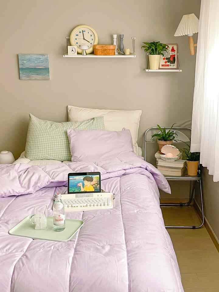 ナチュラルな色調の寝室、ライトブラウンの床と淡い紫色の寝具が配置された雰囲気のある空間