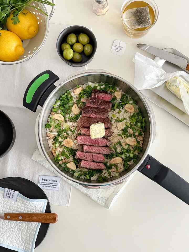 ナチュラルカラーと透明素材が調和したキッチンのテーブルに完成した土鍋ご飯と皿、レモン、オリーブが美しく配置された印象的な空間