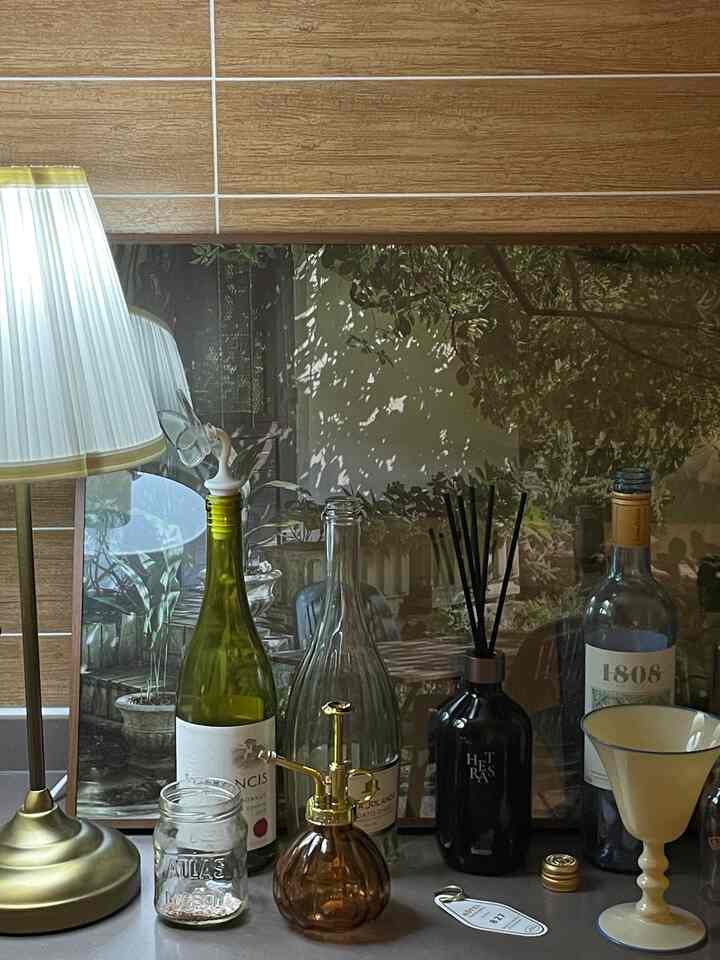 ナチュラルとグリーンの色調の室内、広い額縁とテーブルランプ、ディフューザー、ワインボトルが配置されたおうちカフェの雰囲気