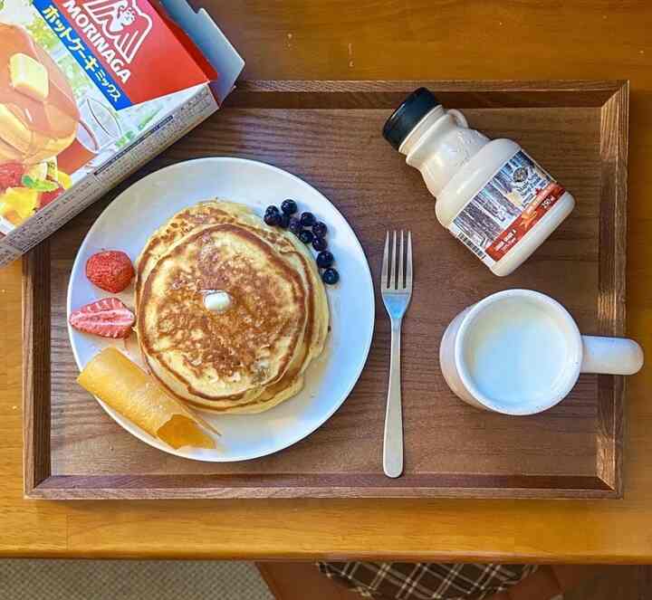 木目調の長方形トレイにパンケーキとフルーツ、マグカップ、シロップボトルが置かれたおうちカフェ風のデザートセッティング