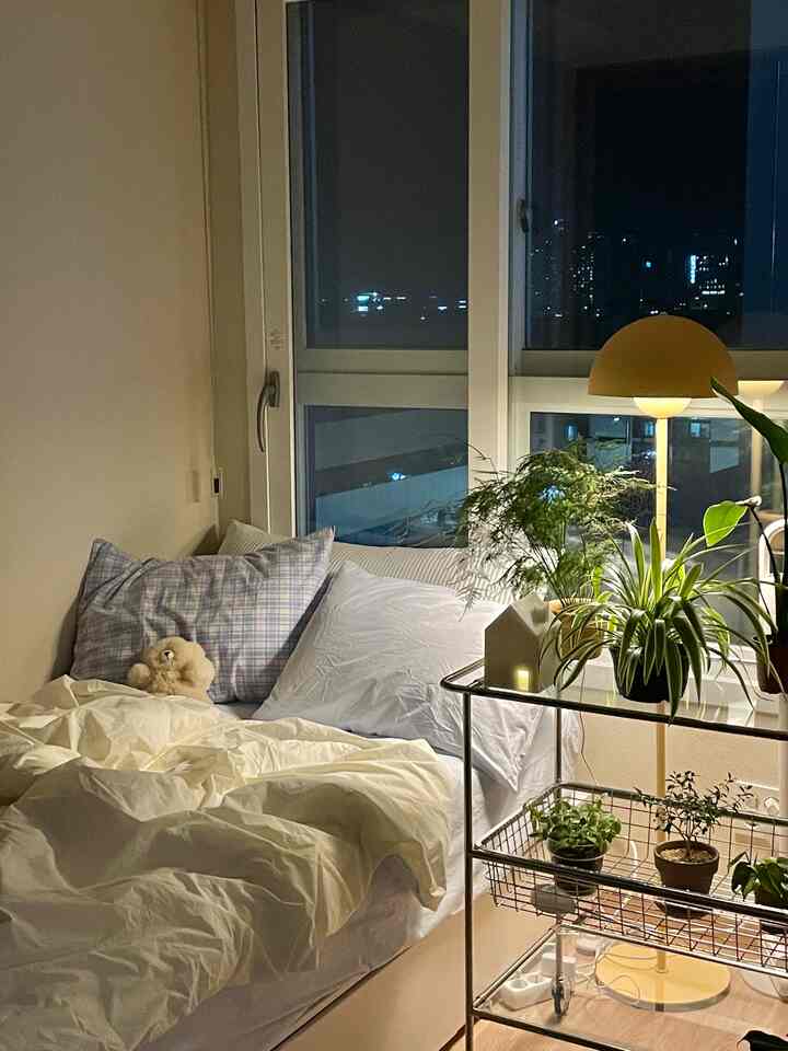 白とベージュの落ち着いた色調の寝室、窓際に植物が配置されたナチュラルモダンなインテリア