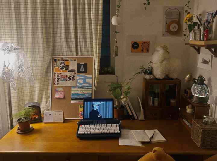 ベージュとナチュラルな色調のホームオフィス、木製デスクにノートパソコンと植物、文房具が配置された雰囲気のある空間