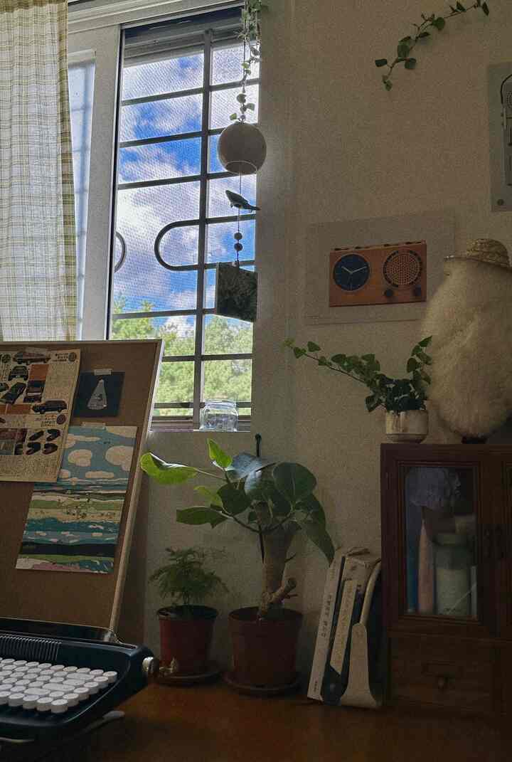 明るい空が見える窓と植物が配置されたナチュラルヴィンテージスタイルの落ち着いた書斎空間
